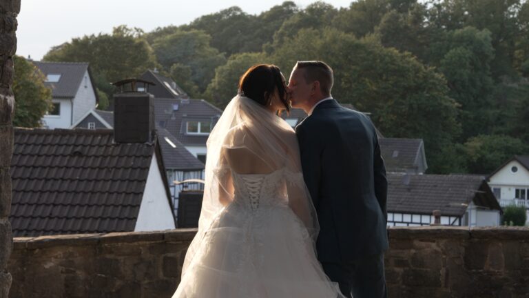 Hochzeitskleid und Anzug des Paares bei einem Kuss vor dem Eingang der Burg Blankenstein